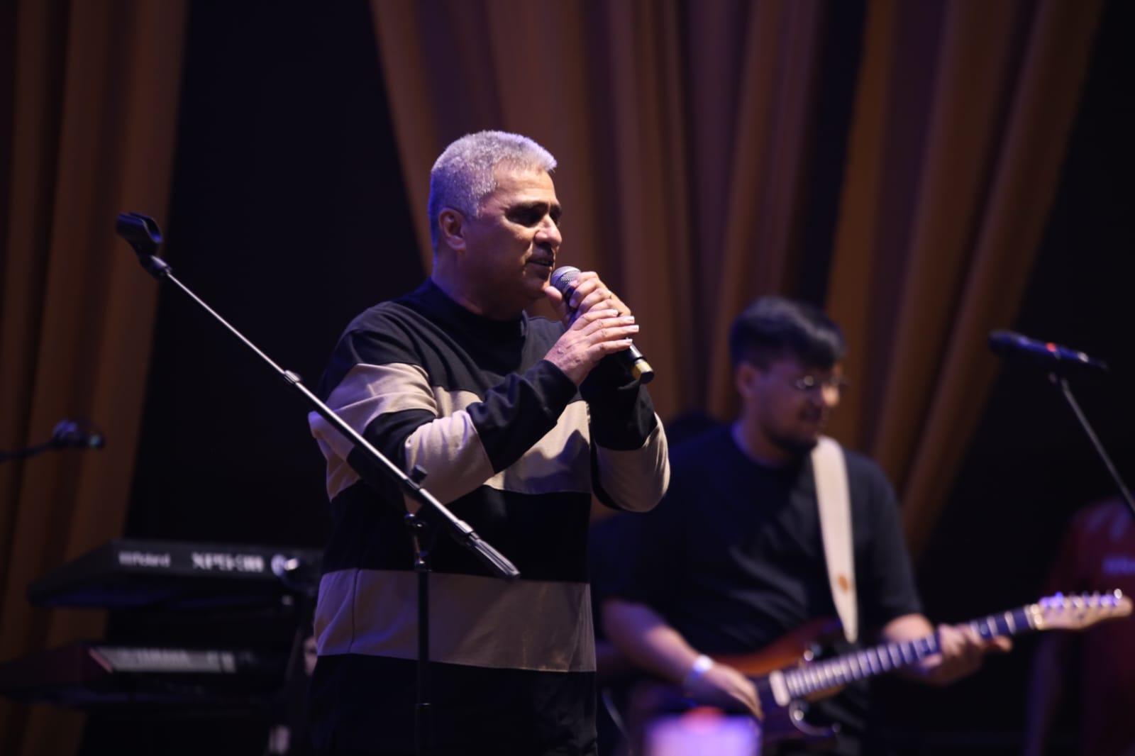 Vocalista ao microfone, com guitarrista e teclado ao fundo